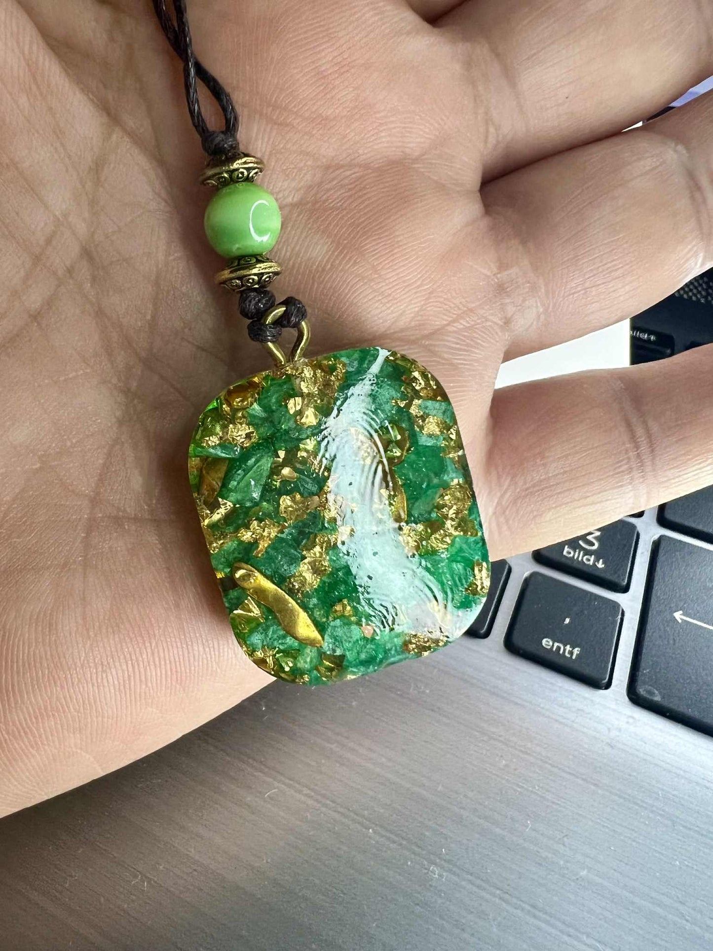 Anhänger Halskette aus grünem Kunstharz mit goldfarbenen Einlagen und einem filigranen Lebensbaum-Motiv. Der Baum des Lebens