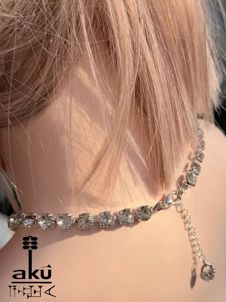Rückseite der Halskette mit der Verlängerungskette und dem kleinen Herzanhänger. Glitzernde Steine im Licht auf Haut und Mannequin