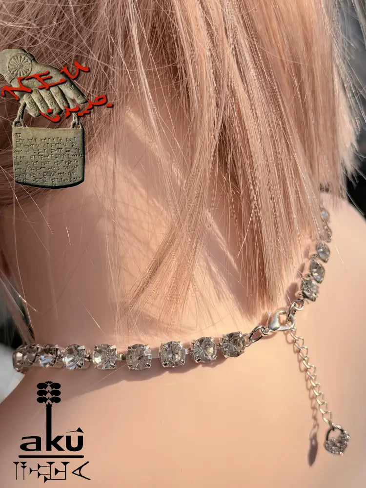 Rückseite der Halskette mit der Verlängerungskette und dem kleinen Herzanhänger. Glitzernde Steine im Licht auf Haut und Mannequin